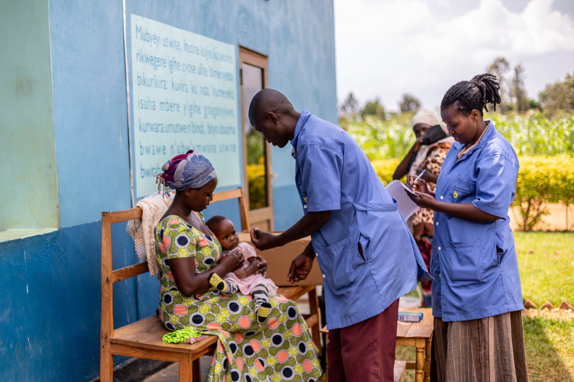 Two health care workers are attending to a mother holding her baby.